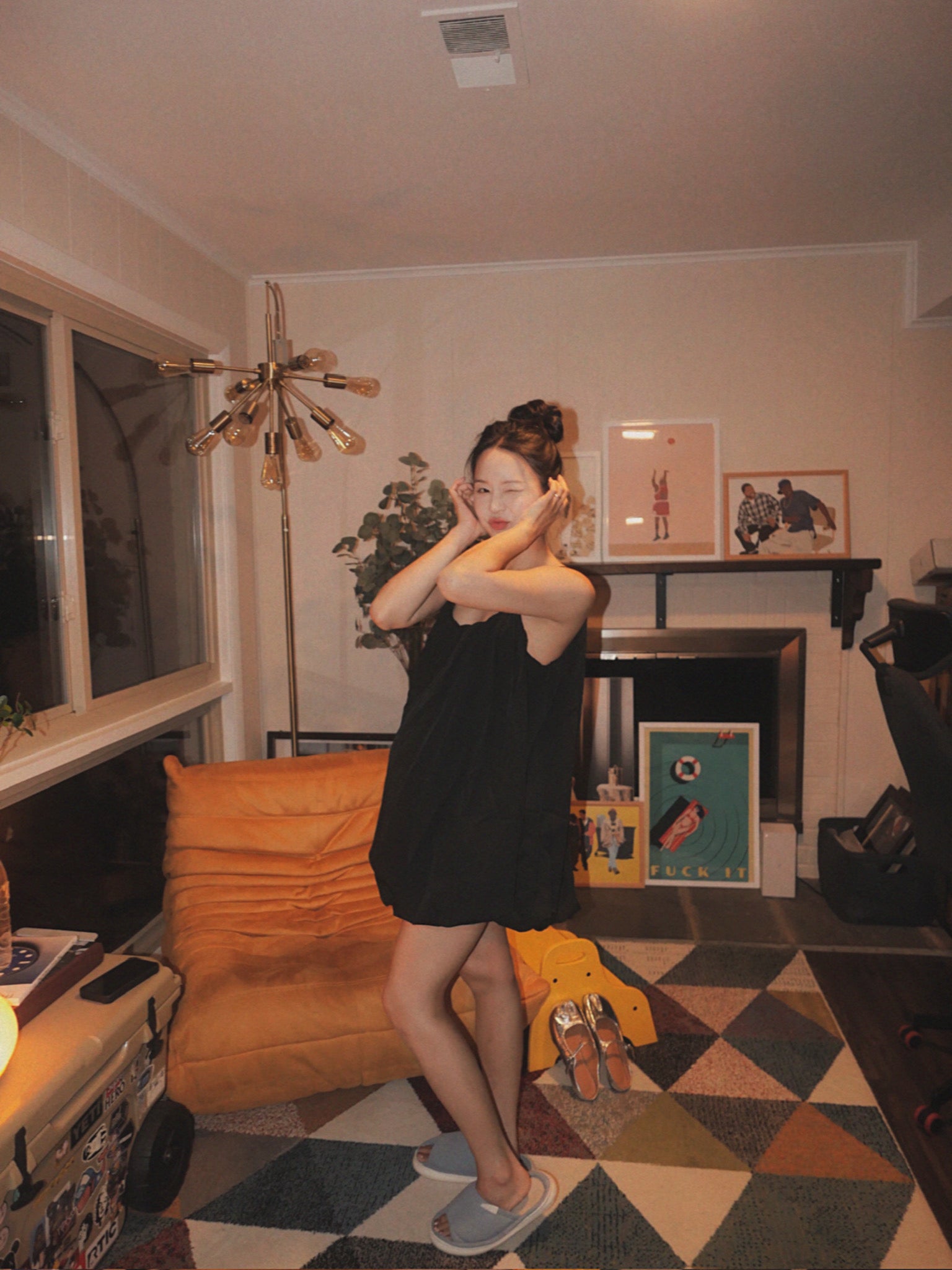 Woman in a black dress standing in a living room with decor and furniture.