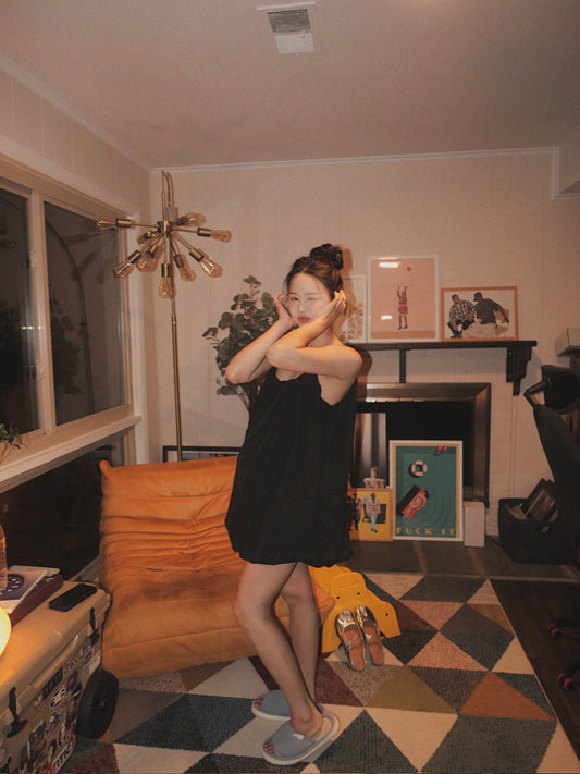 Woman in a black dress standing in a living room with decor and furniture.